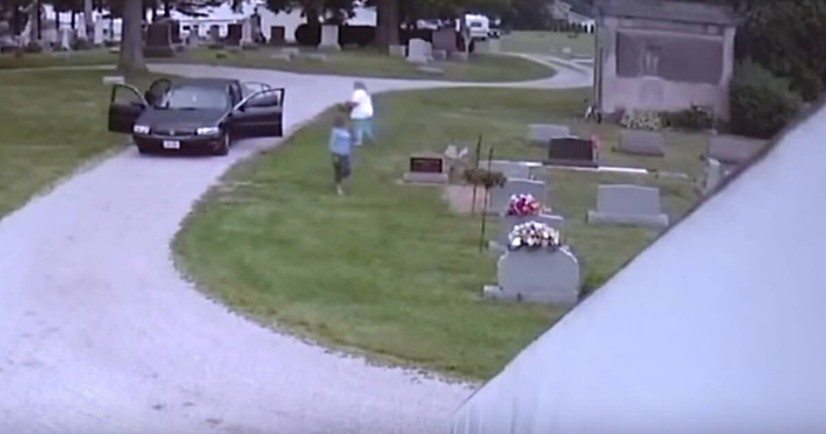 Women approach tombstone thinking no one can see, only there's a camera trained on them